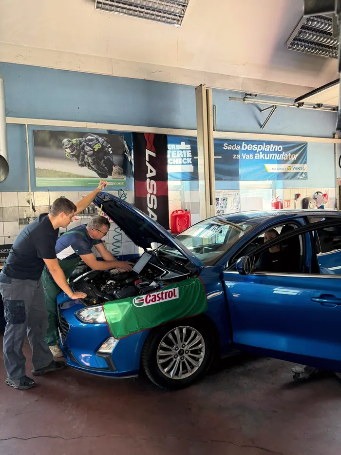 Dva mehaničara nad otvorenim motorom plavog automobila, dijagnostika preko računala